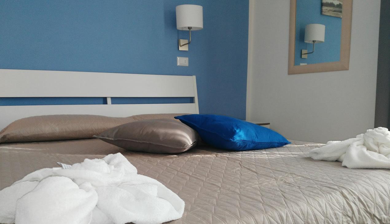 Camera da letto moderna con parete blu, cuscini colorati e accappatoi sul letto.