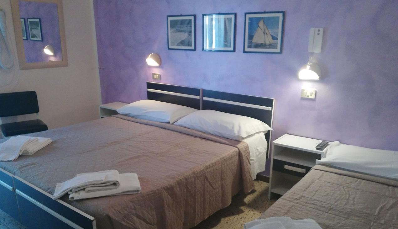 Camera d'albergo con letto matrimoniale, pareti viola e decorazioni nautiche.