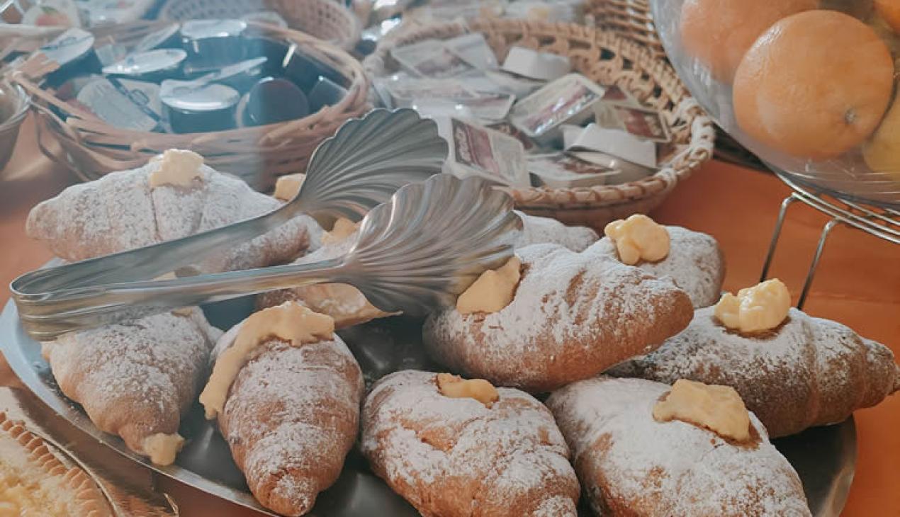 Buffet con cornetti, marmellate, succhi e frutta per una colazione ricca.