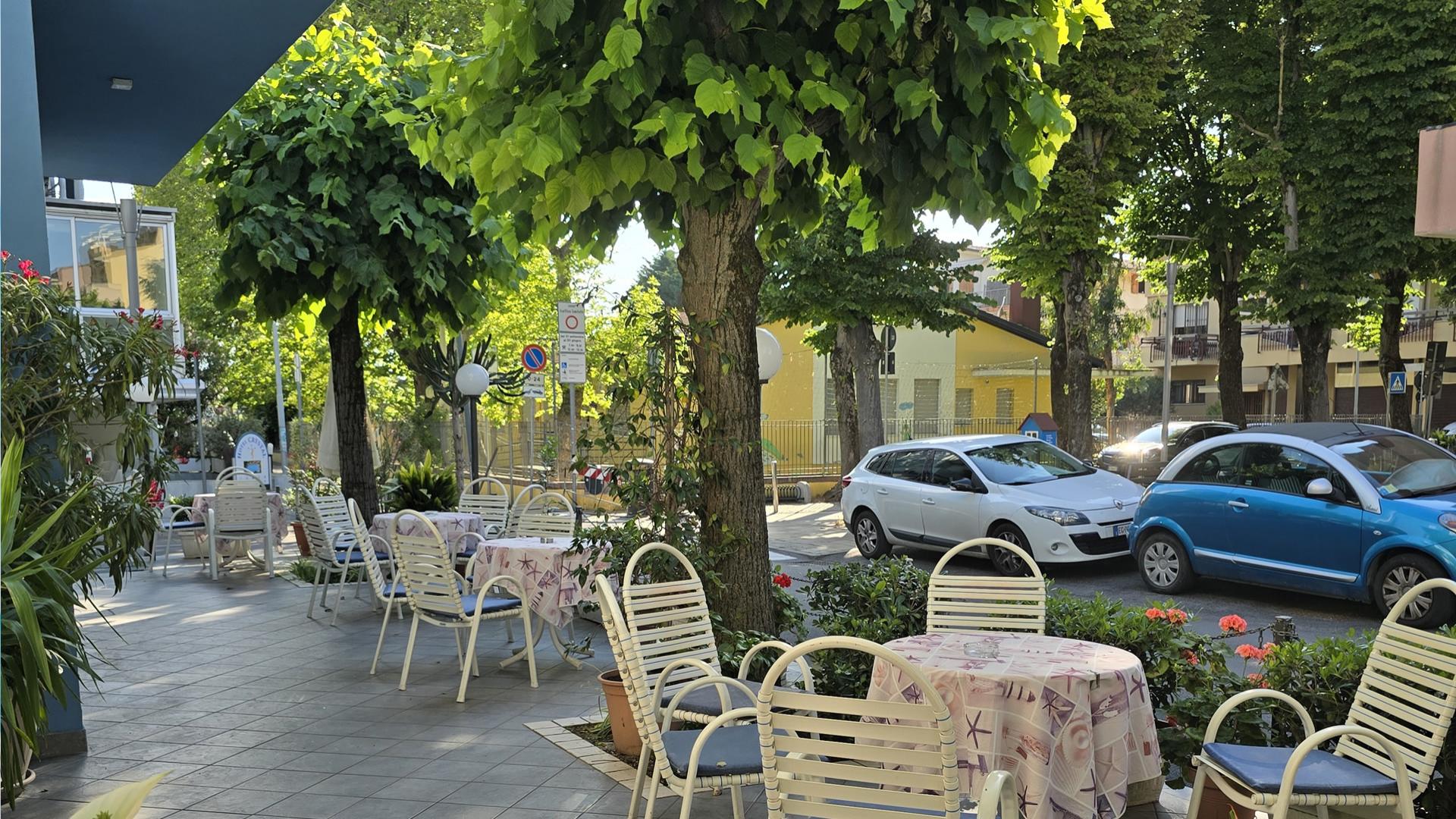 Edificio blu a tre piani con balconi, alberi e cielo sereno.