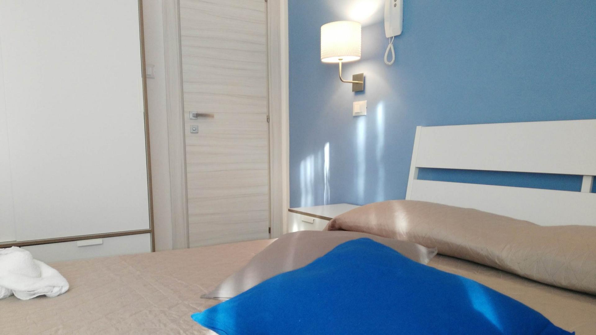 Camera da letto moderna con pareti blu, lampada da parete e cuscini colorati.