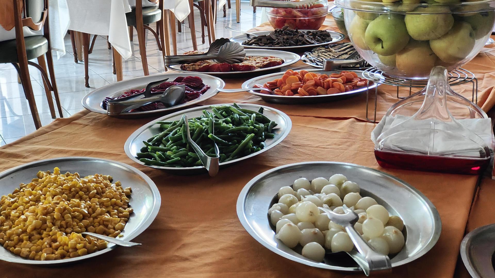 Buffet con verdure, frutta e insalate su tavoli apparecchiati con tovaglie arancioni.