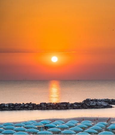 Tramonto sul mare con ombrelloni blu e scogliere in lontananza.