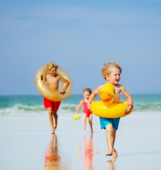 Bambini felici giocano sulla spiaggia con ciambelle gonfiabili colorate.