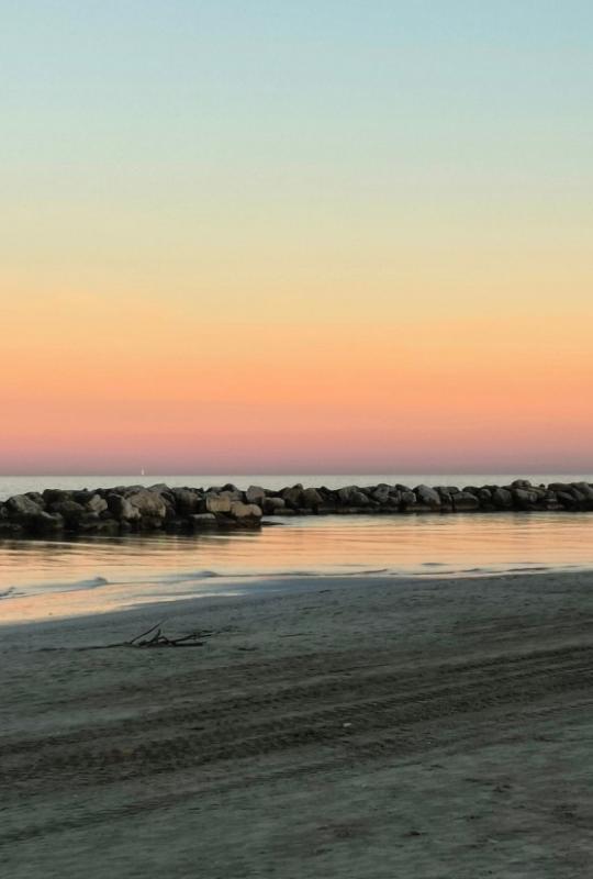 Tramonto sul mare con cielo sfumato e scogli lungo la riva.