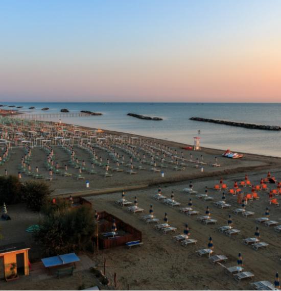 Spiaggia al tramonto con lettini e ombrelloni vuoti, mare calmo in lontananza.