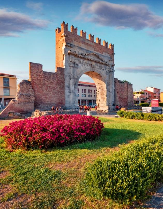 Arco di Augusto a Rimini, antico monumento romano con fiori in primo piano.