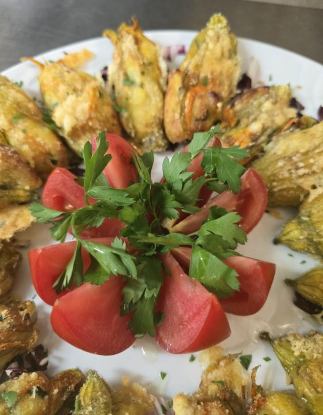 Fiori di zucca fritti con decorazione di pomodori e prezzemolo su piatto.