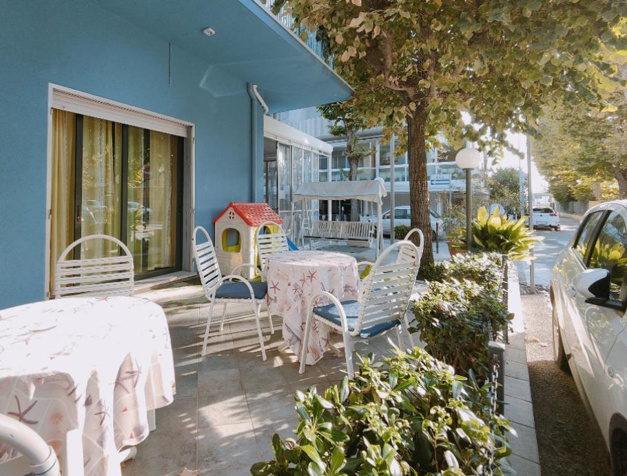 Terrazza con tavoli apparecchiati, sedie bianche e giochi per bambini, vicino a un'auto parcheggiata.