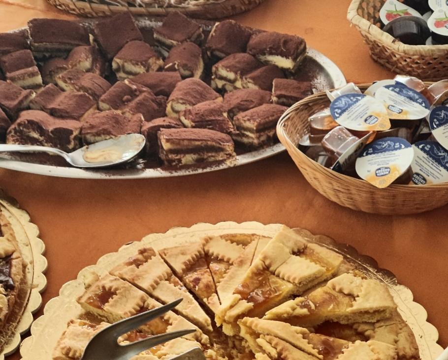 Dolci vari: tiramisù, crostata e marmellate su un tavolo.