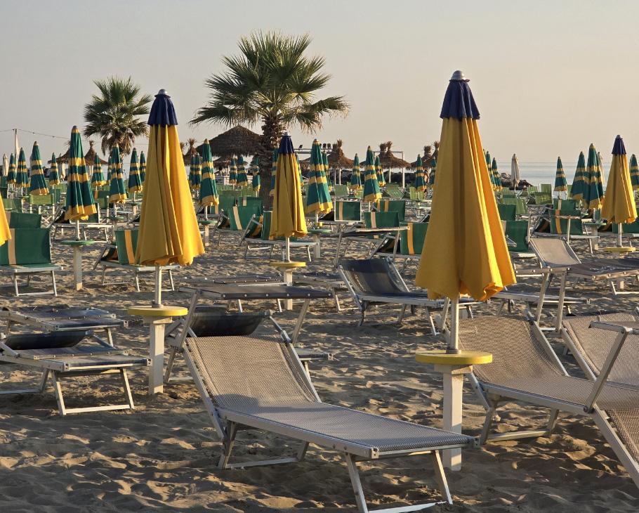 Spiaggia con ombrelloni gialli e verdi, lettini e palme al tramonto.