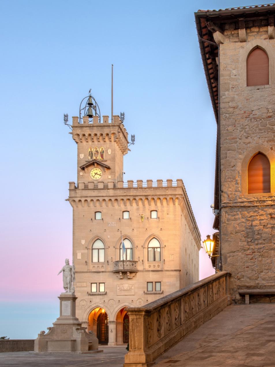 Palazzo Pubblico a San Marino al tramonto, con torre e statua in primo piano.