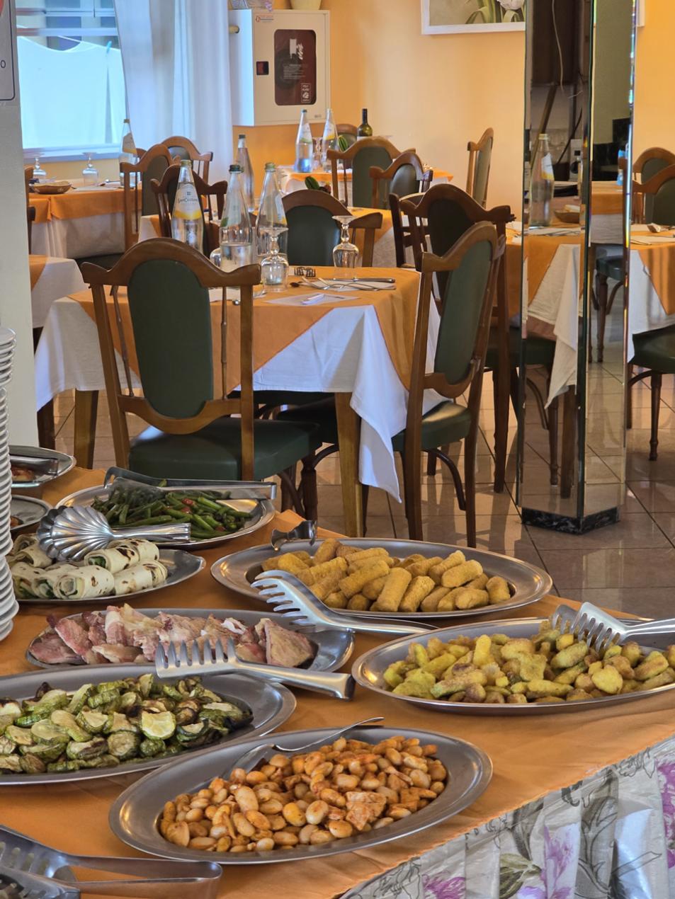 Buffet con piatti di verdure, patatine e salsicce in un ristorante luminoso.