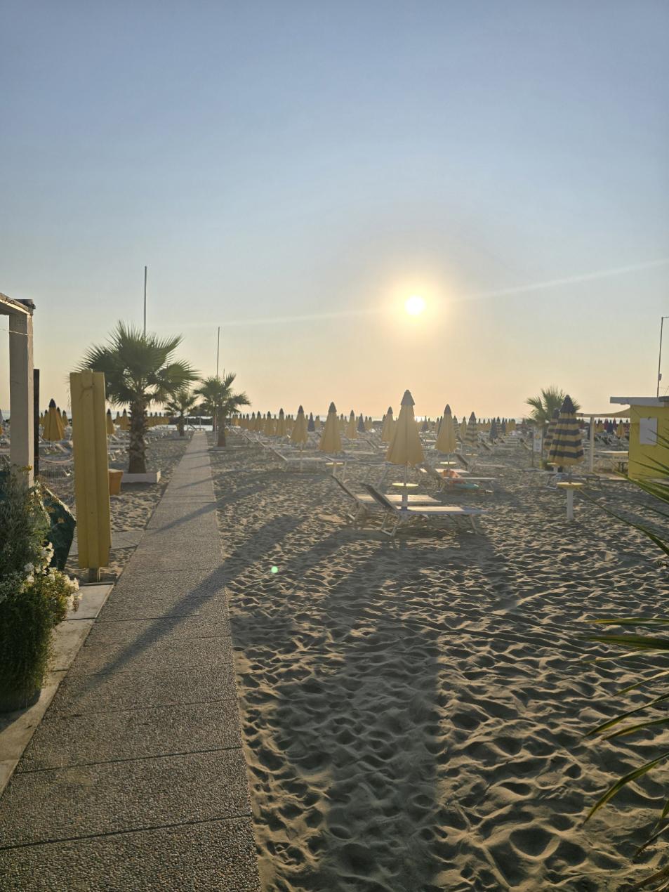 Spiaggia al tramonto con ombrelloni chiusi e passerella tra la sabbia.